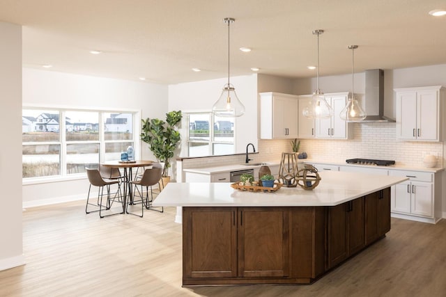 kitchen featuring wall chimney exhaust hood, white cabinets, a center island, and gas stovetop