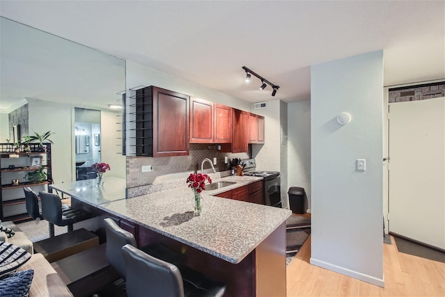 kitchen with kitchen peninsula, backsplash, electric range, a breakfast bar, and sink