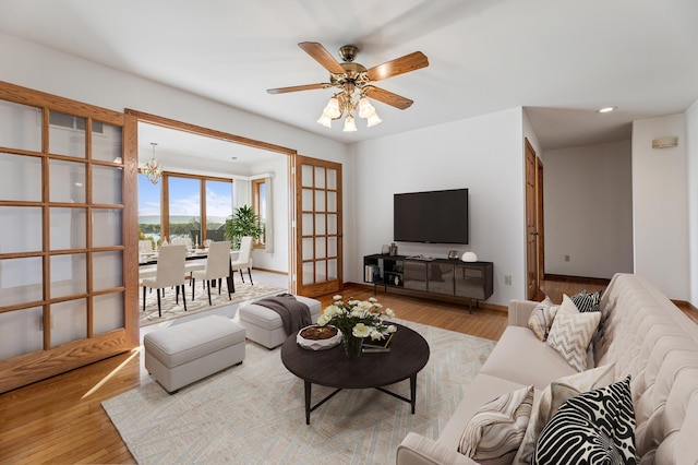 living room featuring french doors, light hardwood / wood-style flooring, and ceiling fan with notable chandelier