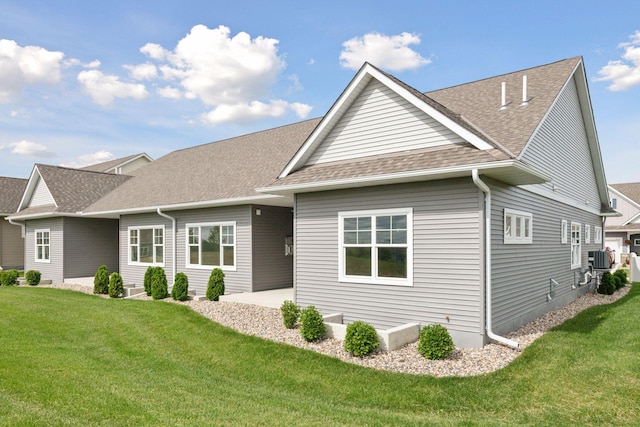 view of front facade with a patio area, a shingled roof, a front yard, and cooling unit