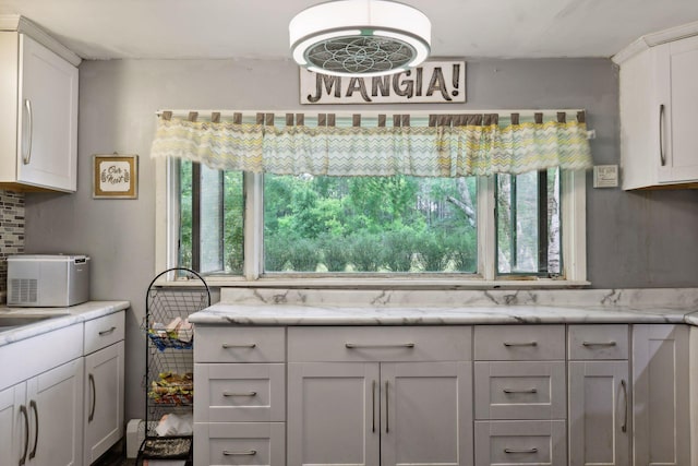 kitchen with backsplash, light stone counters, and white cabinetry