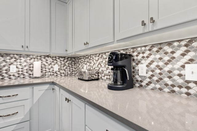 kitchen with tasteful backsplash, light stone countertops, and white cabinets