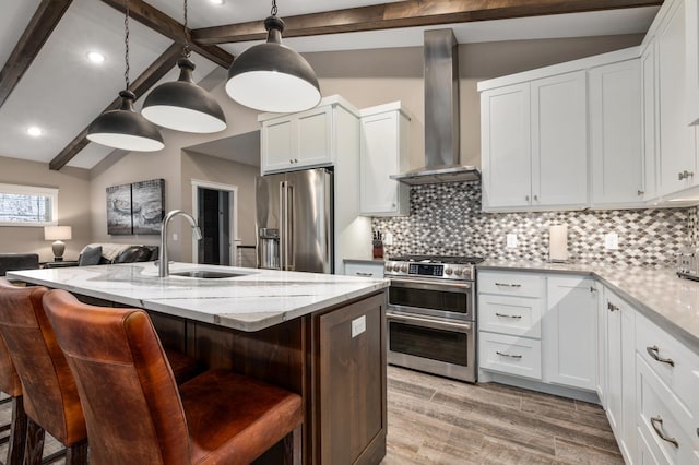 kitchen with wall chimney range hood, a breakfast bar, hanging light fixtures, stainless steel appliances, and white cabinets