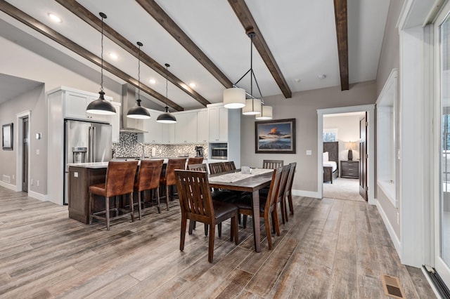 dining area with light wood-type flooring and vaulted ceiling with beams