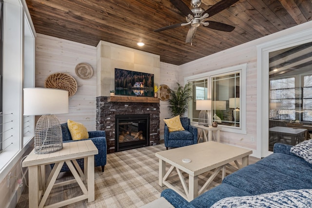 living room with ceiling fan, wooden ceiling, wooden walls, and a fireplace