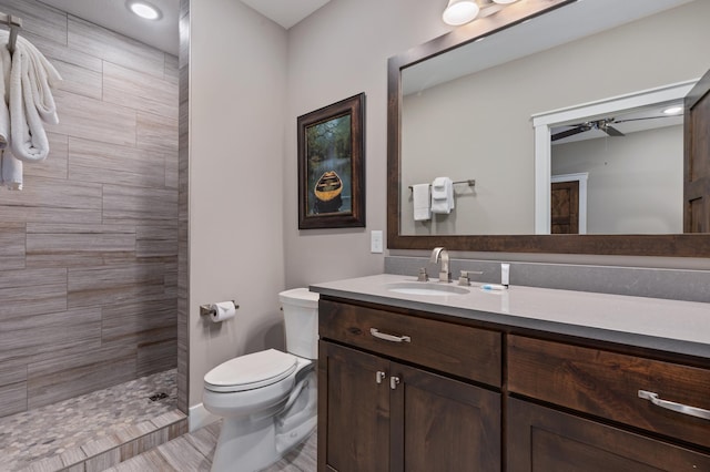 bathroom with ceiling fan, vanity, toilet, and a tile shower