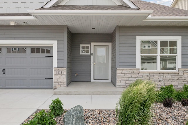 property entrance with a shingled roof, stone siding, and a garage