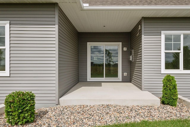 entrance to property with a patio area and a shingled roof