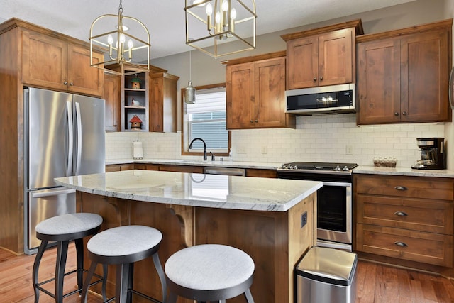 kitchen with a center island, pendant lighting, stainless steel appliances, brown cabinetry, and light stone countertops