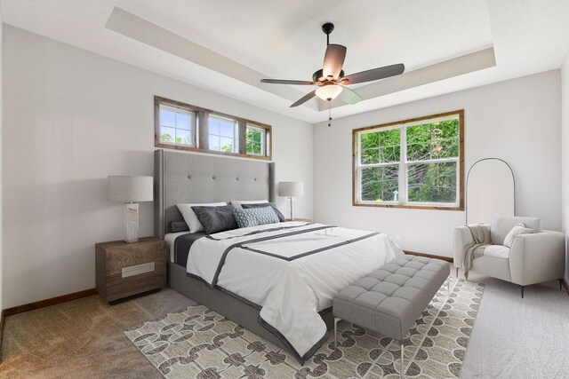 bedroom with a raised ceiling, multiple windows, ceiling fan, and light carpet