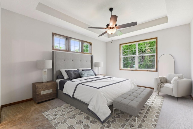 carpeted bedroom with a raised ceiling and ceiling fan