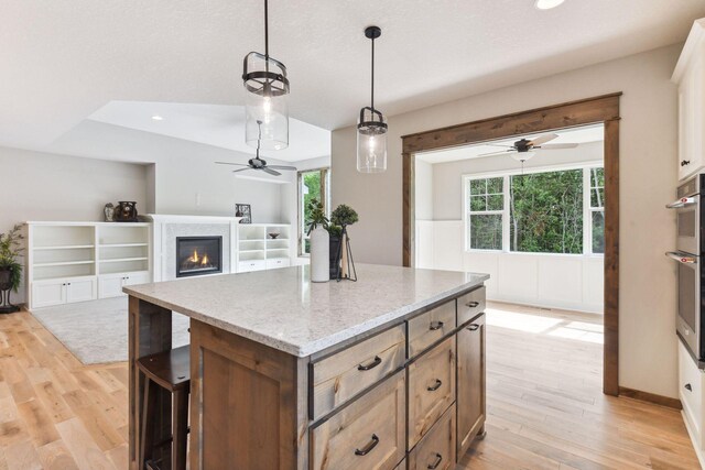 kitchen featuring pendant lighting, a center island, light wood-type flooring, plenty of natural light, and light stone counters