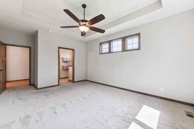 unfurnished bedroom with ceiling fan, light colored carpet, ensuite bath, and a raised ceiling