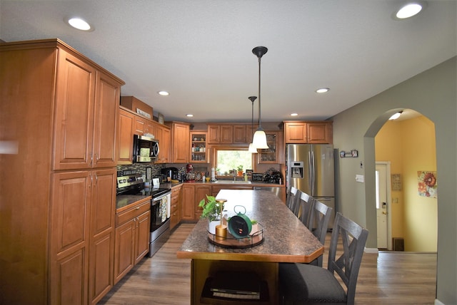 kitchen with brown cabinetry, arched walkways, appliances with stainless steel finishes, and dark countertops