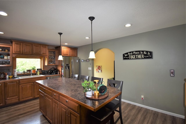 kitchen featuring a kitchen breakfast bar, stainless steel refrigerator with ice dispenser, dark countertops, arched walkways, and a sink