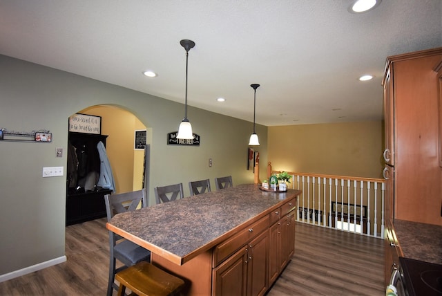 kitchen featuring dark wood-style flooring, dark countertops, a kitchen breakfast bar, electric stove, and arched walkways