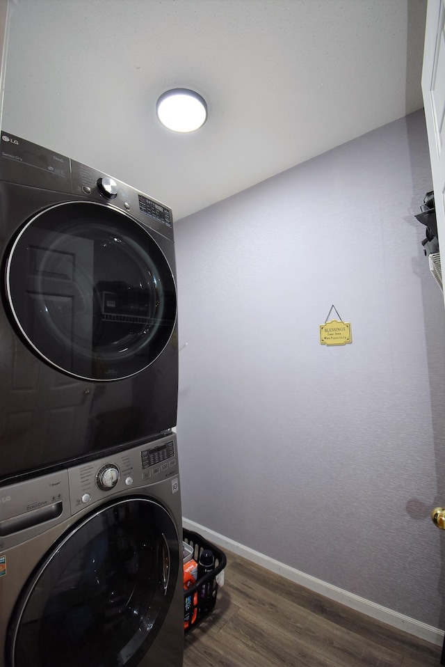 clothes washing area with baseboards, laundry area, stacked washing maching and dryer, and wood finished floors