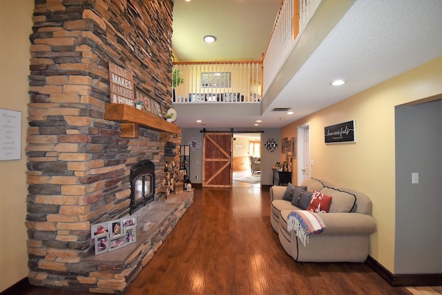 living room with a stone fireplace, a barn door, wood finished floors, baseboards, and a high ceiling