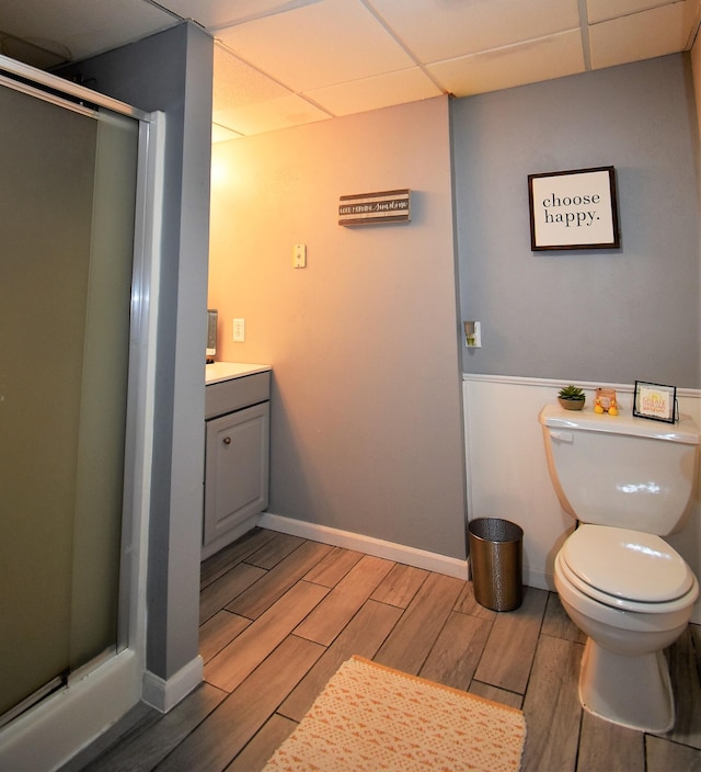 bathroom featuring vanity, toilet, a drop ceiling, a shower stall, and wood tiled floor