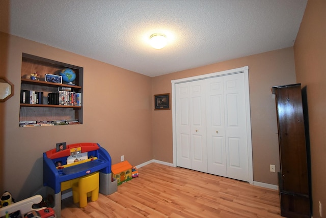 game room featuring a textured ceiling, baseboards, and wood finished floors