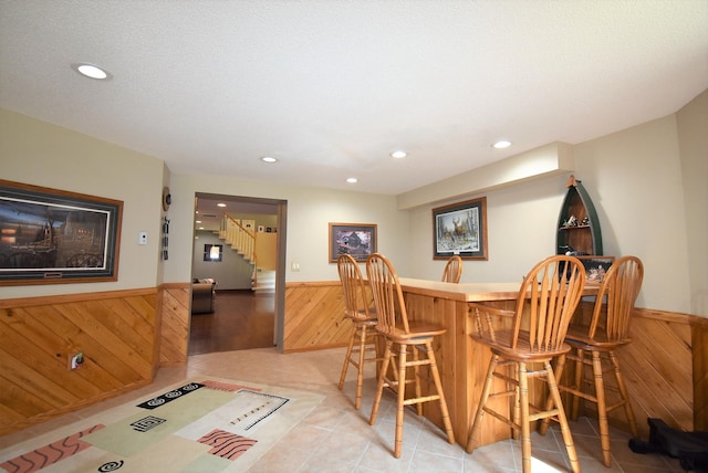dining space with wood walls, a dry bar, stairway, and a wainscoted wall
