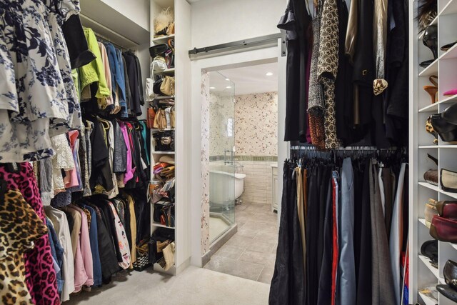 walk in closet with a barn door and light tile patterned floors