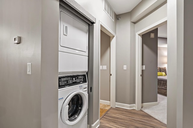 laundry room featuring wood-type flooring and stacked washer / dryer