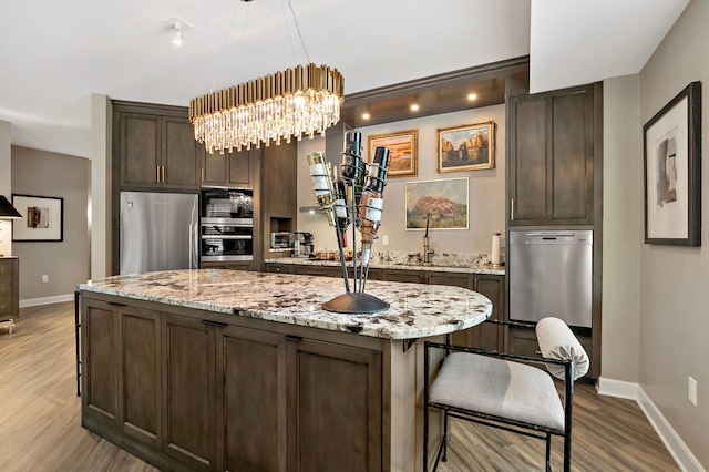 kitchen with light wood-type flooring, a kitchen island, hanging light fixtures, light stone countertops, and stainless steel appliances