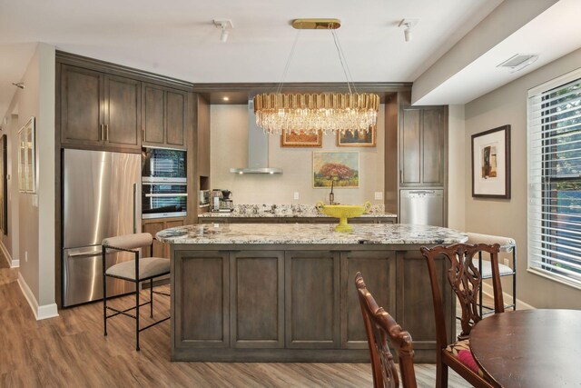 kitchen featuring appliances with stainless steel finishes, hardwood / wood-style flooring, light stone counters, ventilation hood, and hanging light fixtures