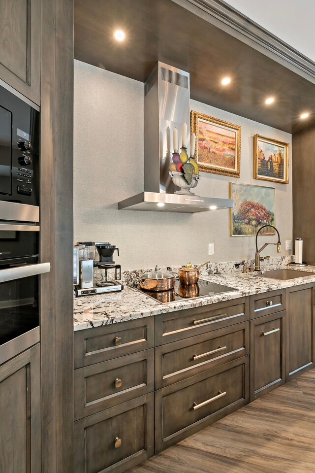 kitchen featuring dark hardwood / wood-style floors, wall chimney exhaust hood, light stone countertops, sink, and black appliances