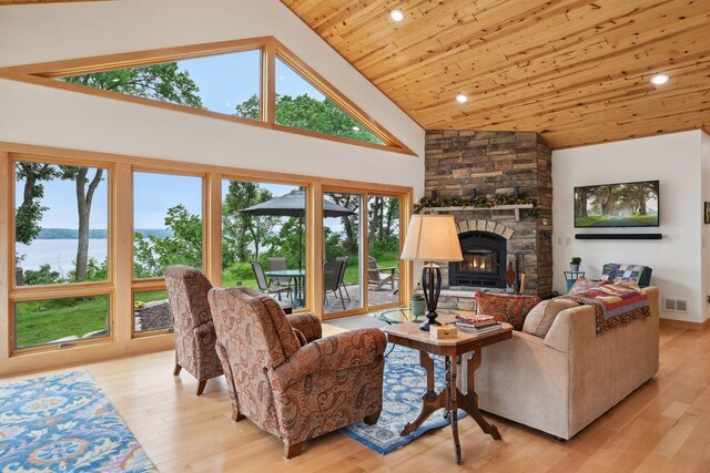 living room featuring wood ceiling, a stone fireplace, light hardwood / wood-style floors, a water view, and high vaulted ceiling