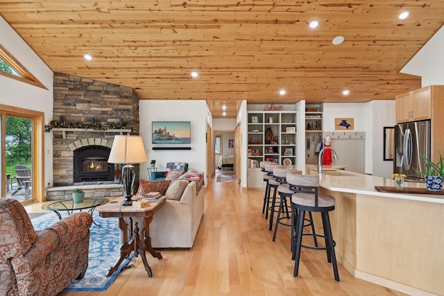 living room with wood ceiling, light hardwood / wood-style floors, a stone fireplace, lofted ceiling, and sink