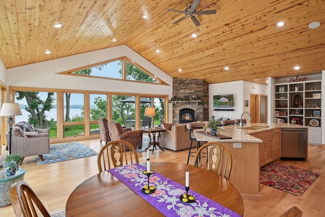 dining area featuring wood ceiling, a stone fireplace, light hardwood / wood-style floors, sink, and high vaulted ceiling