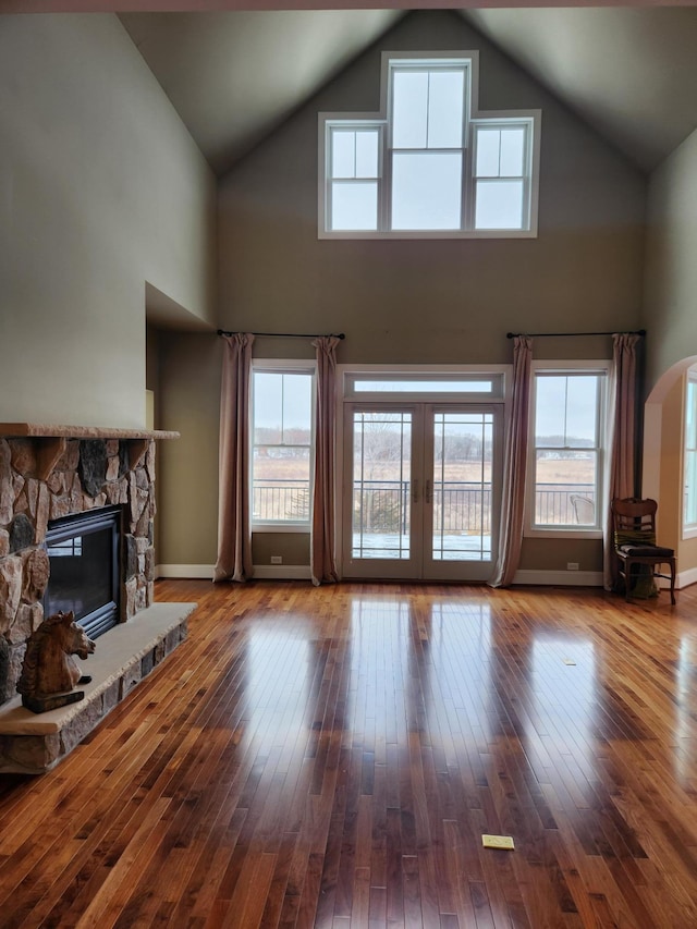 unfurnished living room featuring a stone fireplace, a healthy amount of sunlight, and hardwood / wood-style floors