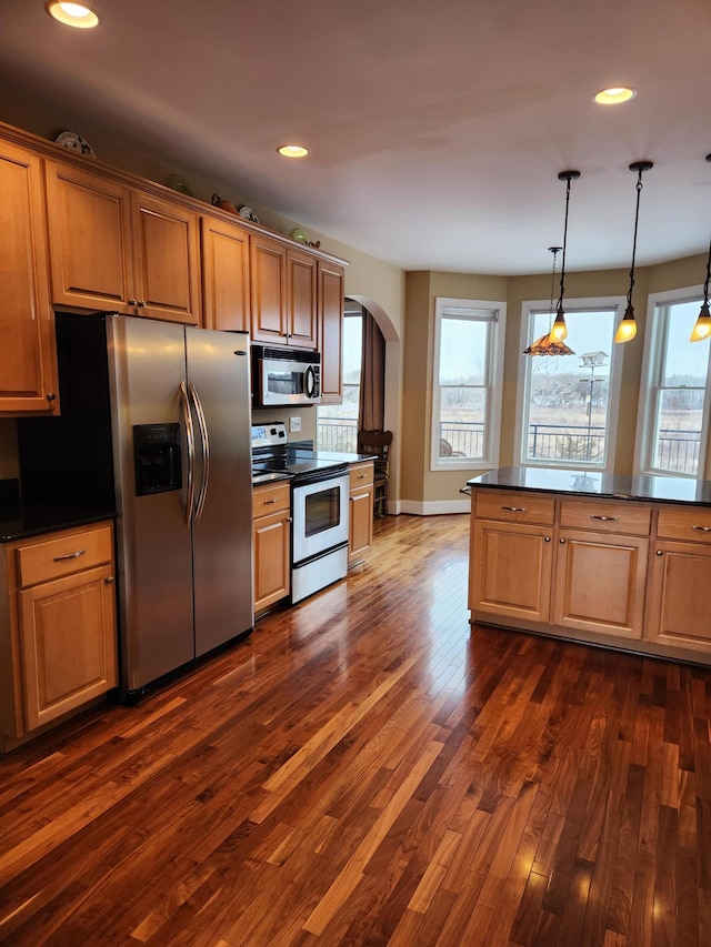 kitchen featuring arched walkways, a healthy amount of sunlight, appliances with stainless steel finishes, dark countertops, and dark wood finished floors