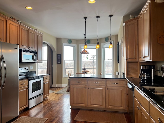 kitchen with arched walkways, a peninsula, appliances with stainless steel finishes, brown cabinetry, and dark countertops