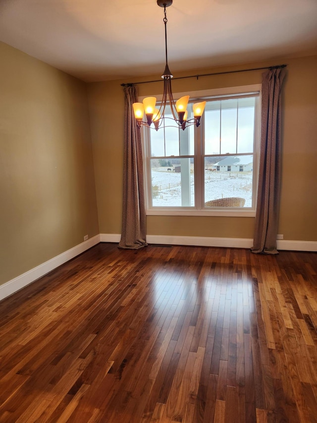 unfurnished room featuring an inviting chandelier, baseboards, and dark wood-type flooring