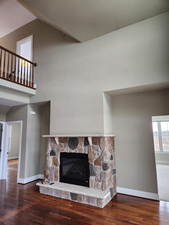 living room featuring a high ceiling, a fireplace, wood finished floors, and baseboards