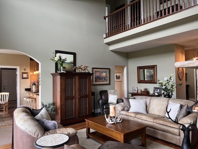 living room with arched walkways, a towering ceiling, and wood finished floors