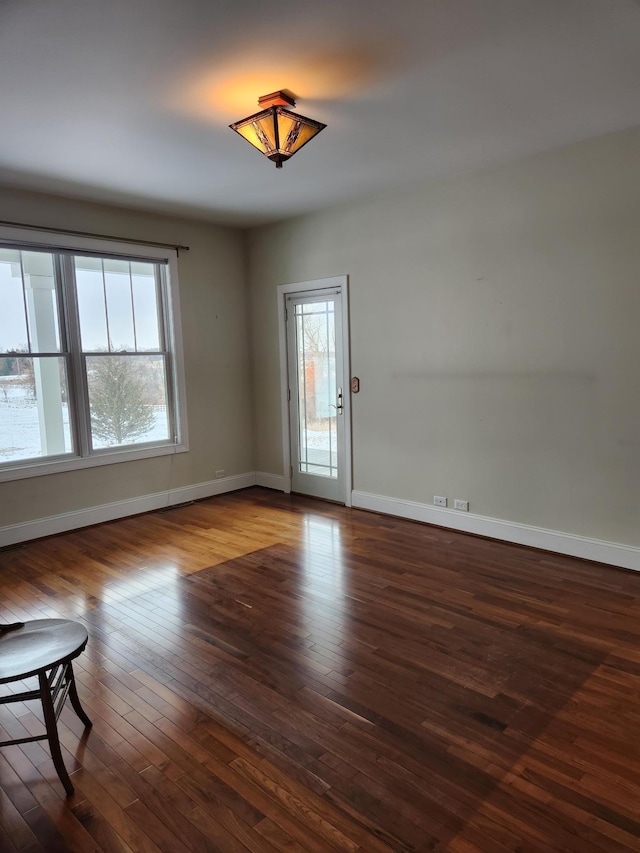 spare room featuring a healthy amount of sunlight, dark wood finished floors, and baseboards