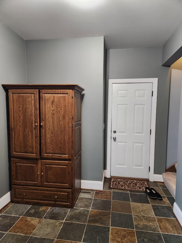 foyer entrance featuring stairway, baseboards, and stone tile flooring