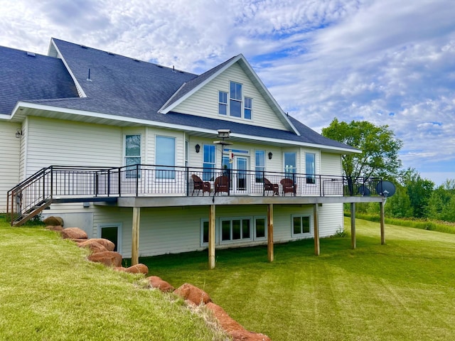 back of house featuring roof with shingles, a lawn, and a wooden deck