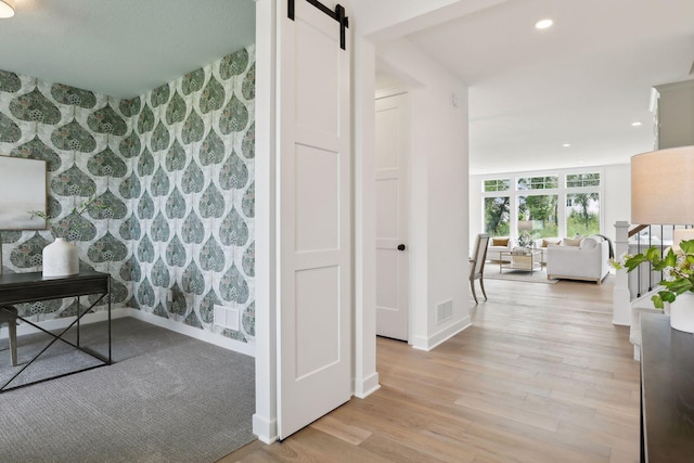 hallway with light hardwood / wood-style floors, expansive windows, and a barn door