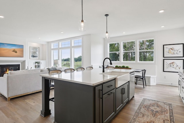 kitchen with hanging light fixtures, dishwasher, an island with sink, and light hardwood / wood-style flooring