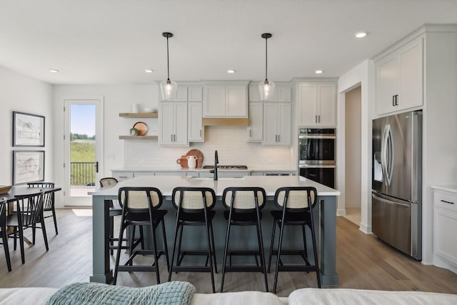 kitchen featuring appliances with stainless steel finishes, an island with sink, white cabinetry, and decorative light fixtures