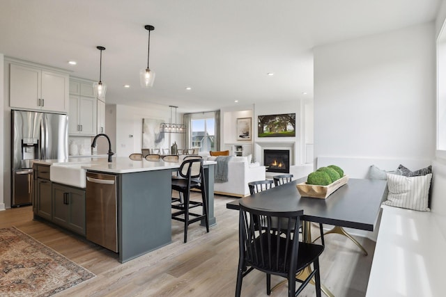 kitchen featuring appliances with stainless steel finishes, decorative light fixtures, gray cabinetry, sink, and a center island with sink