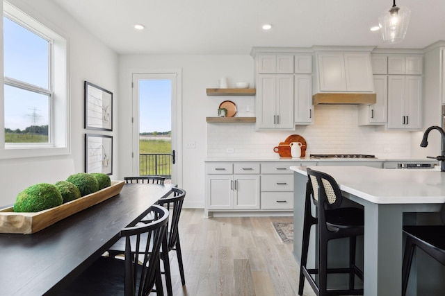 kitchen with stainless steel gas stovetop, a kitchen bar, light hardwood / wood-style floors, decorative light fixtures, and white cabinets