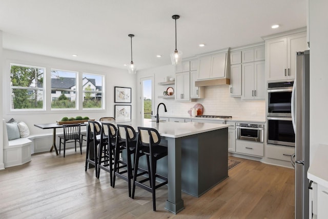 kitchen with decorative light fixtures, sink, white cabinetry, an island with sink, and custom range hood