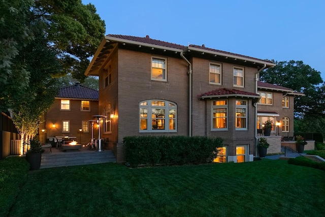 back house at dusk featuring a lawn and a patio area