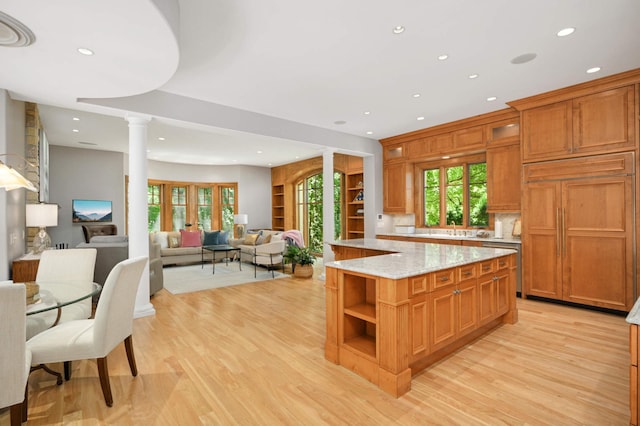 kitchen featuring light wood-type flooring, a kitchen island, paneled built in refrigerator, ornate columns, and light stone countertops